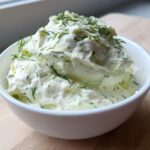 A close-up of creamy, freshly made dill dip topped generously with fresh dill sprigs, served in a white bowl.
