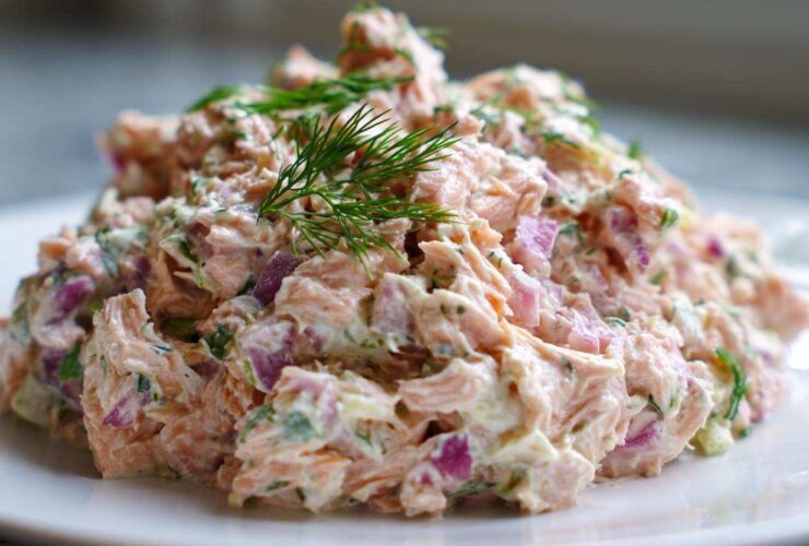 A mound of creamy salmon salad mixed with red onion and herbs, topped with fresh dill.