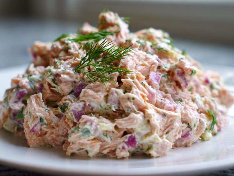 A mound of creamy salmon salad mixed with red onion and herbs, topped with fresh dill.
