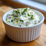 A close-up of creamy homemade tartar sauce recipe garnished with fresh parsley and relish in a white fluted ramekin.