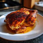 A juicy, whole chicken cooked perfectly in the air fryer, featuring richly seasoned, crispy, dark skin resting in its juices.