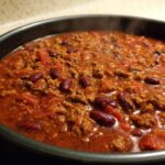 Close-up of steaming, rich chili with ground meat and kidney beans simmering in a dark pot.
