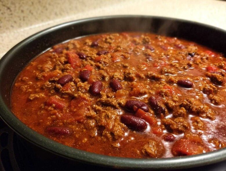 Close-up of steaming, rich chili with ground meat and kidney beans simmering in a dark pot.