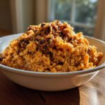 A white bowl filled with mashed, savory orange-colored black eyed peas mixture, served on a wooden surface.