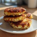 A stack of three golden-brown, pan-fried mashed potato cakes on a white plate.