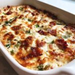 Close-up of a creamy, baked popper dip topped with melted cheese and crispy bacon pieces.