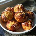 A white bowl filled with freshly baked, golden brown pretzel bites topped with coarse salt.