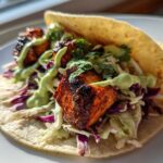 A close-up of a single, delicious salmon taco filled with blackened salmon chunks, purple cabbage slaw, and drizzled with a light green sauce.