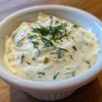 Close-up of creamy homemade tartar sauce garnished with fresh dill in a small white bowl.