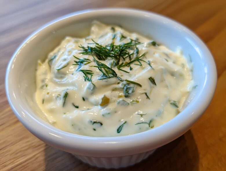 Close-up of creamy homemade tartar sauce garnished with fresh dill in a small white bowl.