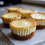 Close-up of several baked mini cheesecake bites with golden brown edges and graham cracker crusts.