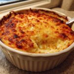 A close-up of a hot, bubbly stuffed mushroom dip in a white ramekin with a browned, cheesy top.