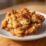 Close-up of a warm slice of apple cobbler recipe showing gooey cinnamon apples and a crumbly brown topping.