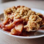 A spoonful of warm, gooey filling and crumbly topping from the best apple cobbler recipe being lifted from a white plate.