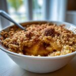 A close-up, appetizing shot of the best apple crumble served in a white bowl with a spoon ready for eating.