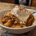 A warm serving of apple crumble topped with melting vanilla ice cream and a dusting of cinnamon.