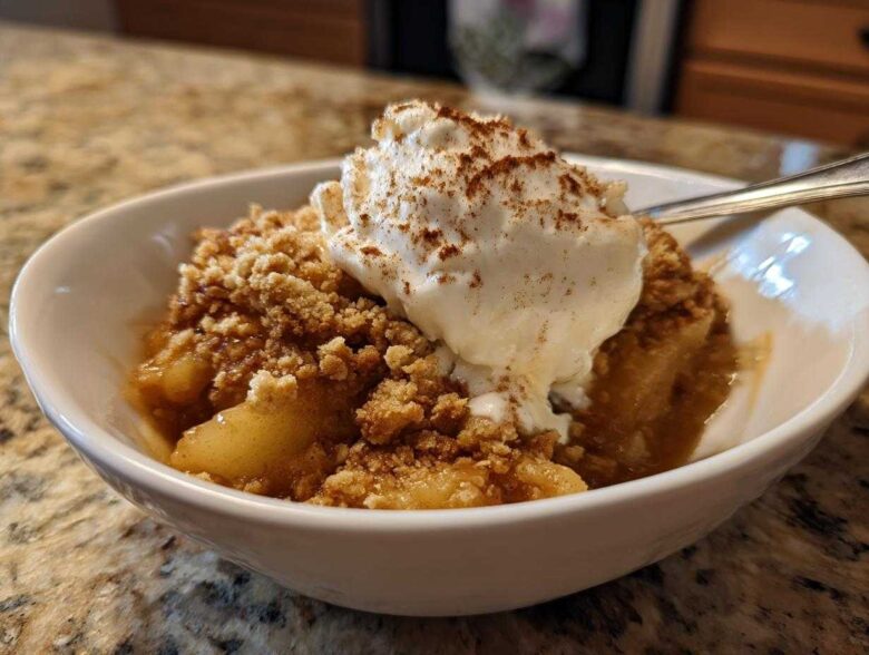 A warm serving of apple crumble topped with melting vanilla ice cream and a dusting of cinnamon.
