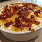 A close-up of a baked jalapeño popper dip in a white ramekin, topped with melted cheese and crispy bacon pieces.