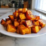 A pile of perfectly caramelized, golden brown roasted sweet potatoes cubes served on a white plate.