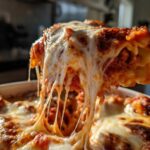 A serving of skillet lasagna is lifted, showing long, melted cheese strings stretching from the pan.