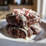 Two stacked, chewy double chocolate peppermint cookies drizzled with white icing and topped with crushed candy canes.