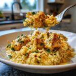 A spoonful of creamy chicken scampi with garlic parmesan rice being lifted from a white bowl.