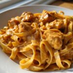 Close-up of fettuccine noodles coated in a rich, orange-hued creamy cajun chicken pasta sauce with chunks of seasoned chicken.