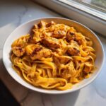 Close-up of creamy cajun chicken pasta featuring fettuccine noodles coated in a rich orange sauce and topped with seasoned chicken pieces.