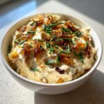 A white bowl filled with creamy caramelized onion dip, topped generously with crispy caramelized onions and fresh green chives.