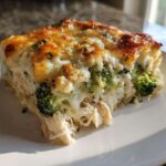 A generous slice of cheesy Chicken Divan casserole featuring shredded chicken and bright green broccoli florets.