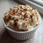 A small white ramekin filled with creamy dip, topped generously with toasted coconut flakes.