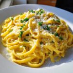 A close-up of a plate piled high with bright yellow Creamy Lemon Pasta, topped with grated cheese and fresh parsley.