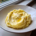 A generous serving of ultra creamy mashed potatoes topped with melted butter and cracked black pepper.