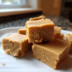 A stack of rich, creamy squares of penuche fudge piled on a white plate, ready to eat.