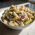 Close-up of creamy pickle pasta salad made with rotini pasta, red onion, and dill, served in a white bowl.