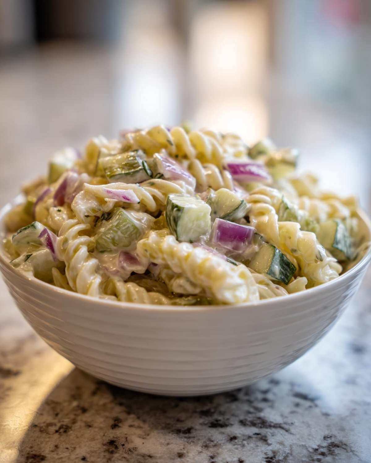 Close-up of creamy pickle pasta salad made with rotini pasta, cucumbers, and red onion in a white bowl.