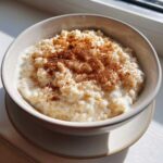 A close-up of a bowl of creamy rice pudding recipe dusted generously with ground cinnamon.