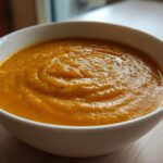 A close-up of a thick, vibrant orange roasted butternut squash soup served in a white bowl.