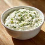 Close-up of creamy homemade tartar sauce topped with fresh dill and chopped green herbs in a white bowl.
