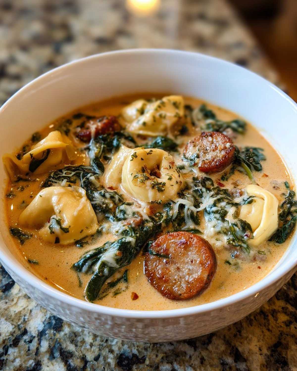 A close-up of creamy tortellini soup filled with cheese tortellini, spinach, and sliced sausage.