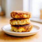 Three golden-brown, crispy mashed potato cakes stacked on a small white plate.