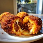 Close-up of crispy, golden brown rice balls cut open to show a gooey cheese and meat filling.