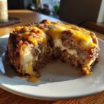 A slice of crockpot french onion meatloaf with melted cheddar and white cheese oozing out, served on a white plate.