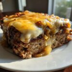 Close-up of a thick slice of crockpot french onion meatloaf topped with melted Swiss cheese and caramelized onions.