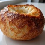 A single, crusty, round bread bowl with the top cut out, ready to be filled.
