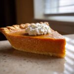A perfect slice of easy pumpkin pie topped with a dollop of fresh whipped cream on a light countertop.