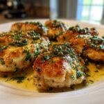 Close-up of several golden-brown chicken piccata fillets swimming in a bright lemon-butter sauce topped with capers and fresh parsley.