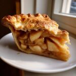 Close-up of a thick slice of amazing apple pie showing a flaky, golden crust and generous cinnamon-spiced apple filling.