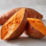 Close-up of a baked sweet potatoes cut in half, revealing the fluffy, bright orange interior.