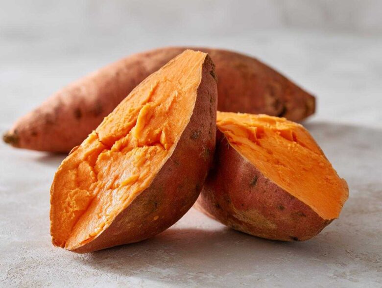 Close-up of a baked sweet potatoes cut in half, revealing the fluffy, bright orange interior.